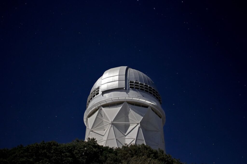A telescope at an observatory silhouetted against a clear night sky filled with stars.